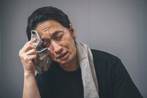 タオルで汗を拭う体調不良の男性