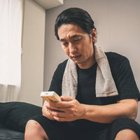 節電中、冷房をつけるか悩む男性、エアコンのリモコンを持つの写真