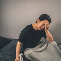 ベッドで頭を押さえる体調不良の男性の写真