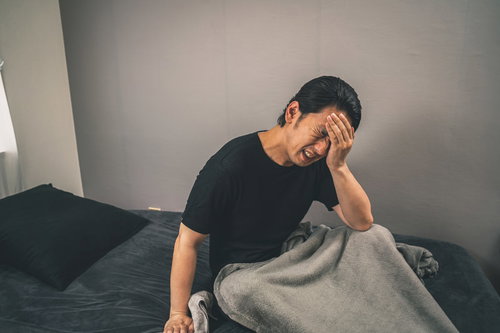 ベッドで頭を押さえる体調不良の男性