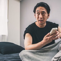 部屋が暑くて冷房をつけるリモコン操作をする男性の写真