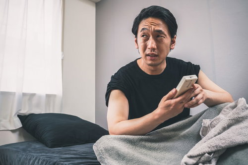 部屋が暑くて冷房をつけるリモコン操作をする男性