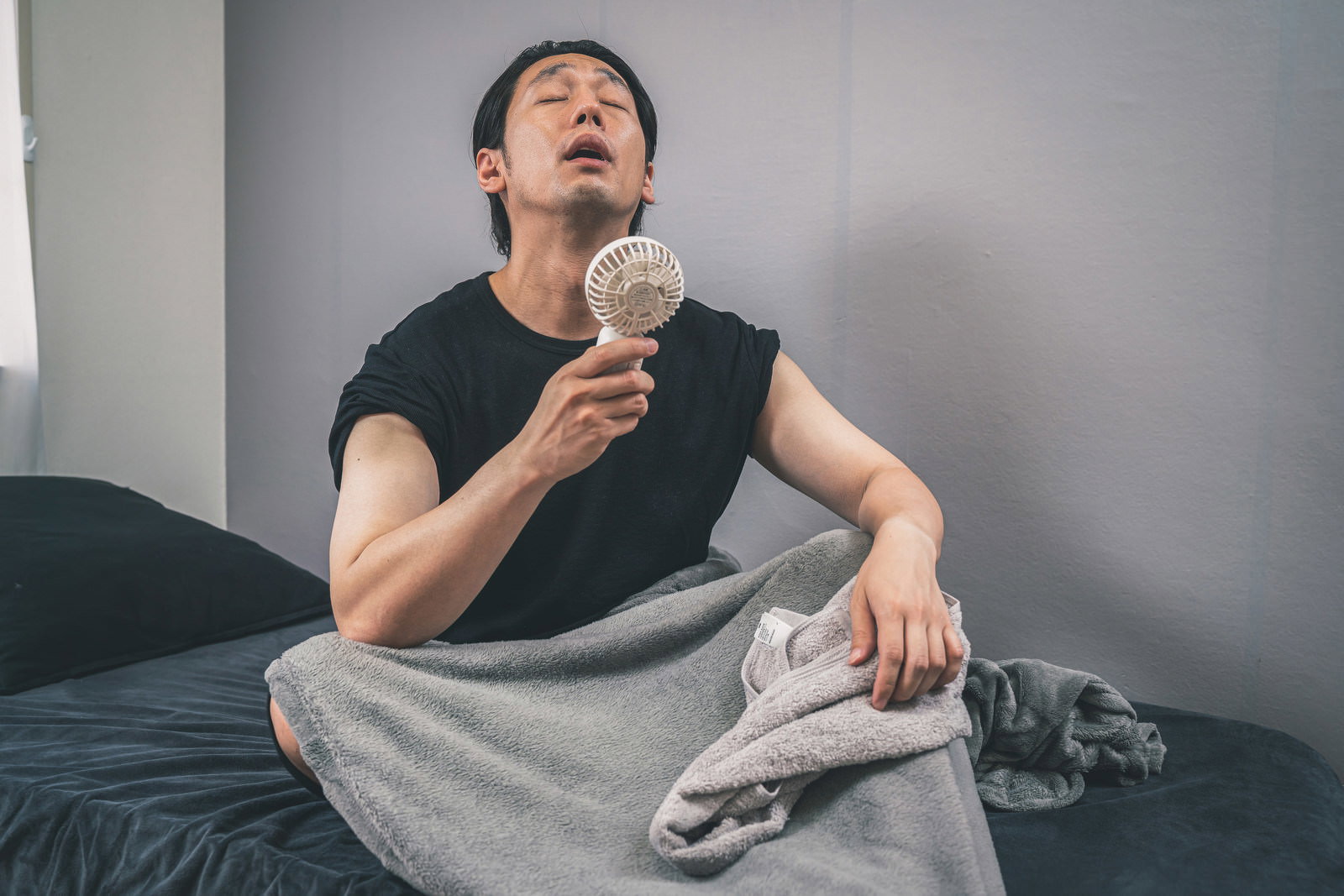 黒いTシャツを着た男性がグレーのハンディ扇風機で涼む［モデル：大川竜弥］