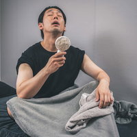 節電対策でハンディ扇風機を使って涼む男性の写真
