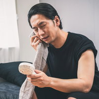 ハンディ扇風機で涼む黒いTシャツの男性の熱中症対策の写真
