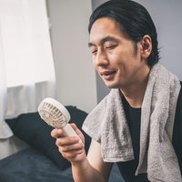 風呂上がりにハンディ扇風機で涼む男性の写真