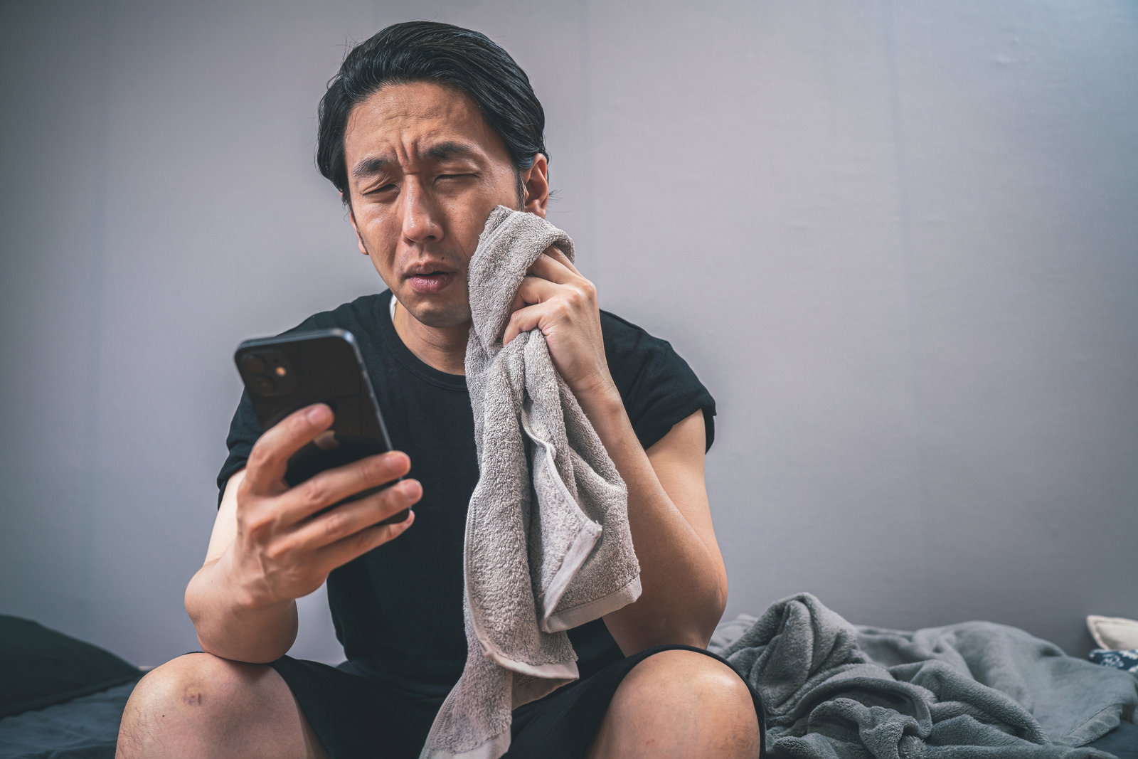 タオルで汗を拭きながらスマートフォンで天気予報を確認する男性［モデル：大川竜弥］