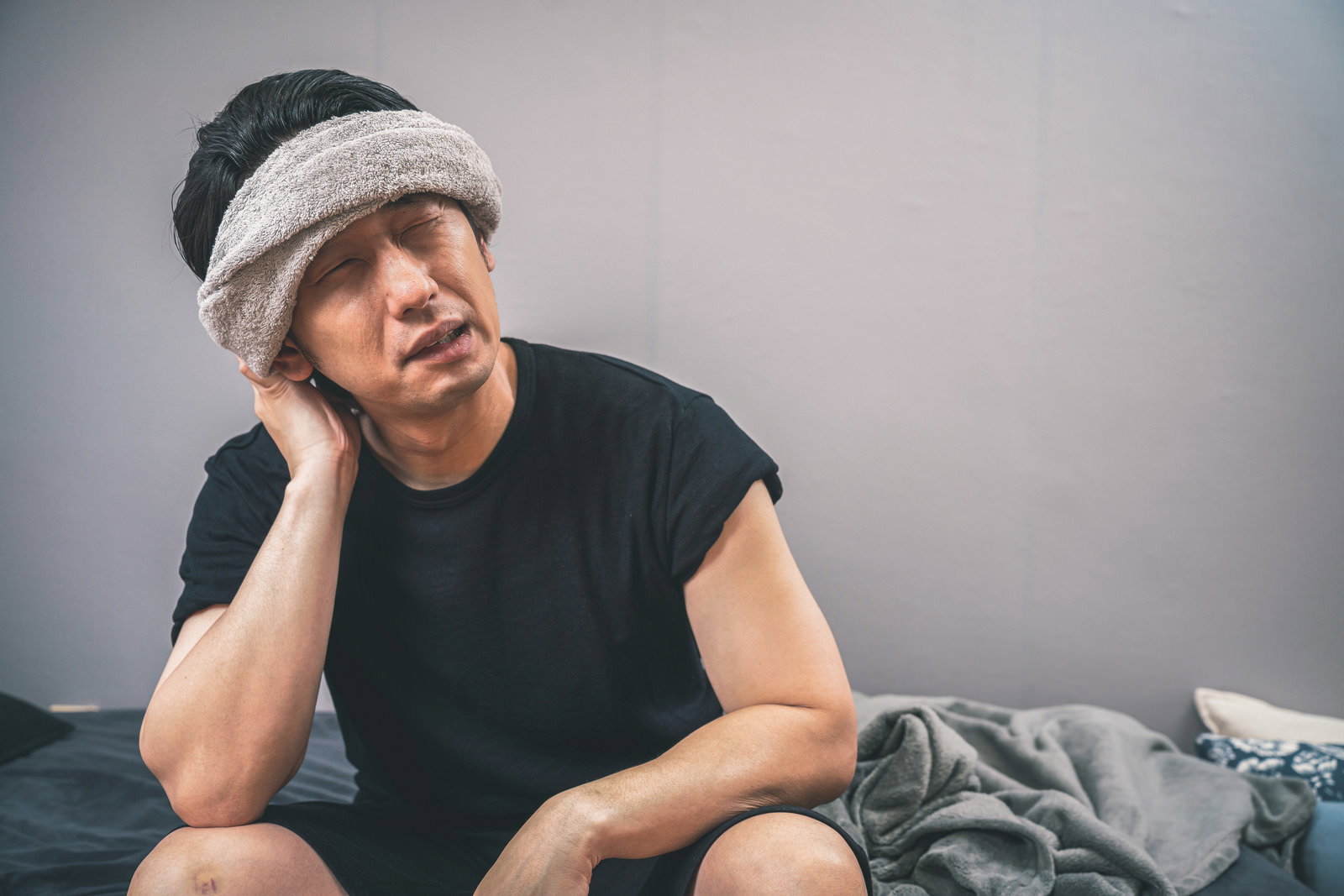 ハチマキを巻いた男性が暑さで手を額に当てて疲れた表情をしている［モデル：大川竜弥］