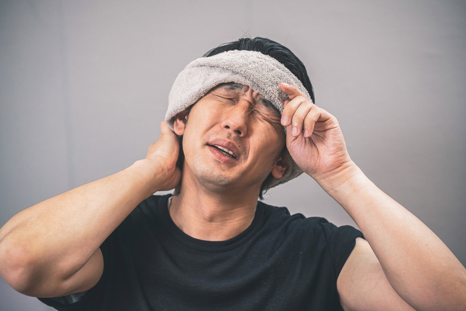 白いハチマキを巻き緑のTシャツを着た男性が額に手を当てて汗を拭っている［モデル：大川竜弥］