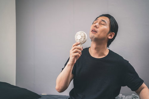 室内で白いハンディ扇風機を使って涼む男性