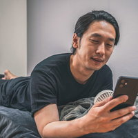 今日の天気予報は猛暑なので家から出たくない、ベッドで寝転ぶ男性の写真