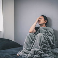 体が冷えて頭が痛い男性、ベッドで頭を抱えるの写真