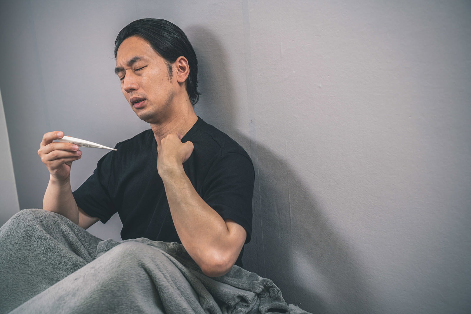 体温計を手に持ち疲れた表情を見せる男性［モデル：大川竜弥］