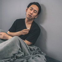 ベッドで体温計を持ち発熱に苦しむ男性の病気休養の写真