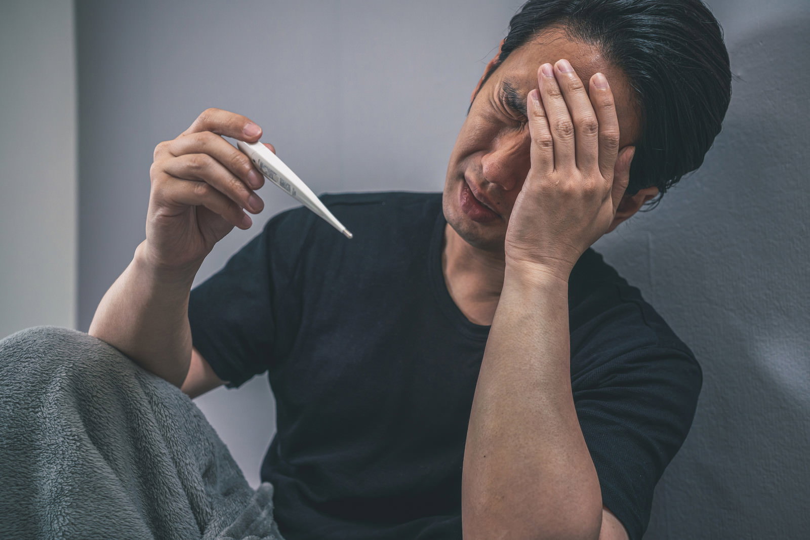 体温計を持ちながら頭を抱えて困った表情をする男性［モデル：大川竜弥］