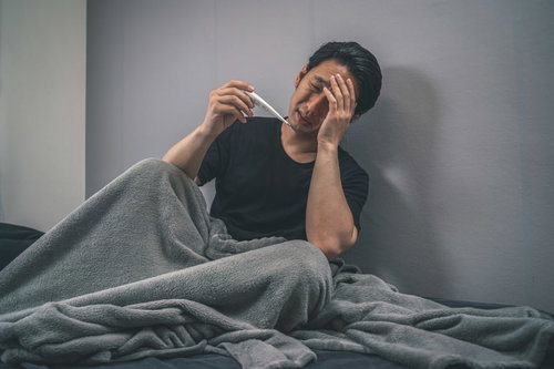 突然の発熱に頭を抱える男性、ベッドで体温計を確認する
