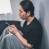 体調不良で職場に連絡をするベッドの男性、体温計を持つの写真