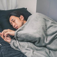 体調不良でもスマホは手放せない男性、ベッドで寝ながら操作の写真