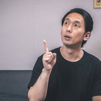 ソファーに座って室内の天井に指をさす男性の写真