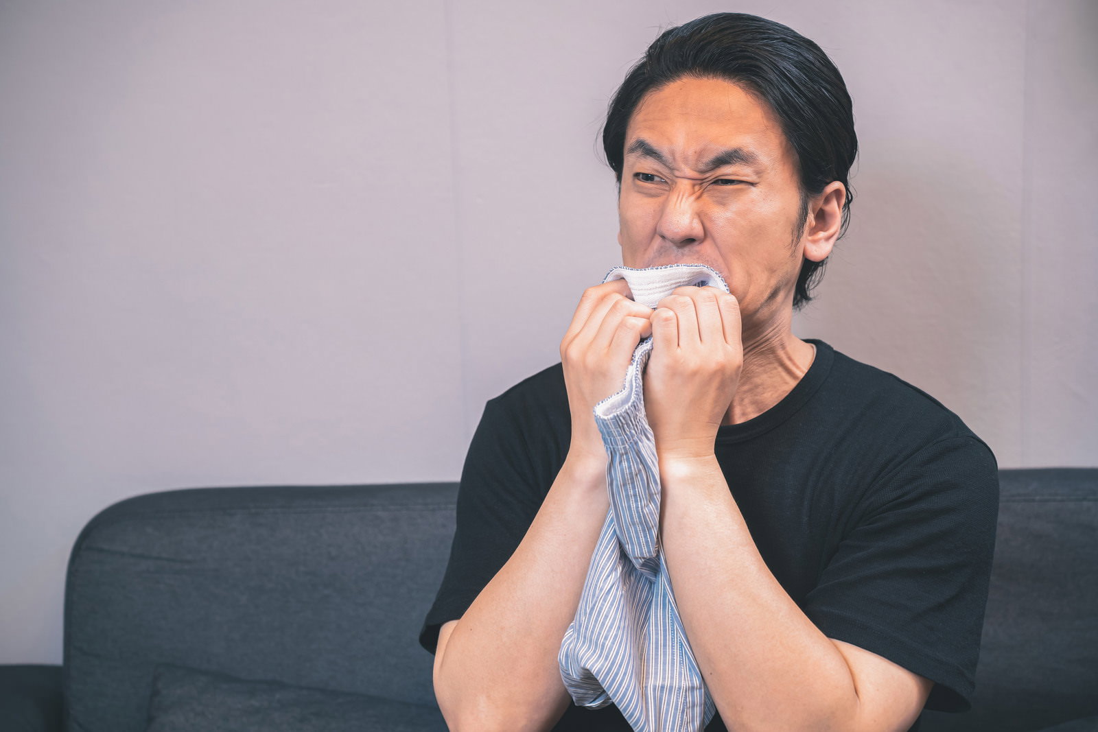 下着のにおいに顔をしかめる黒いTシャツの男性［モデル：大川竜弥］