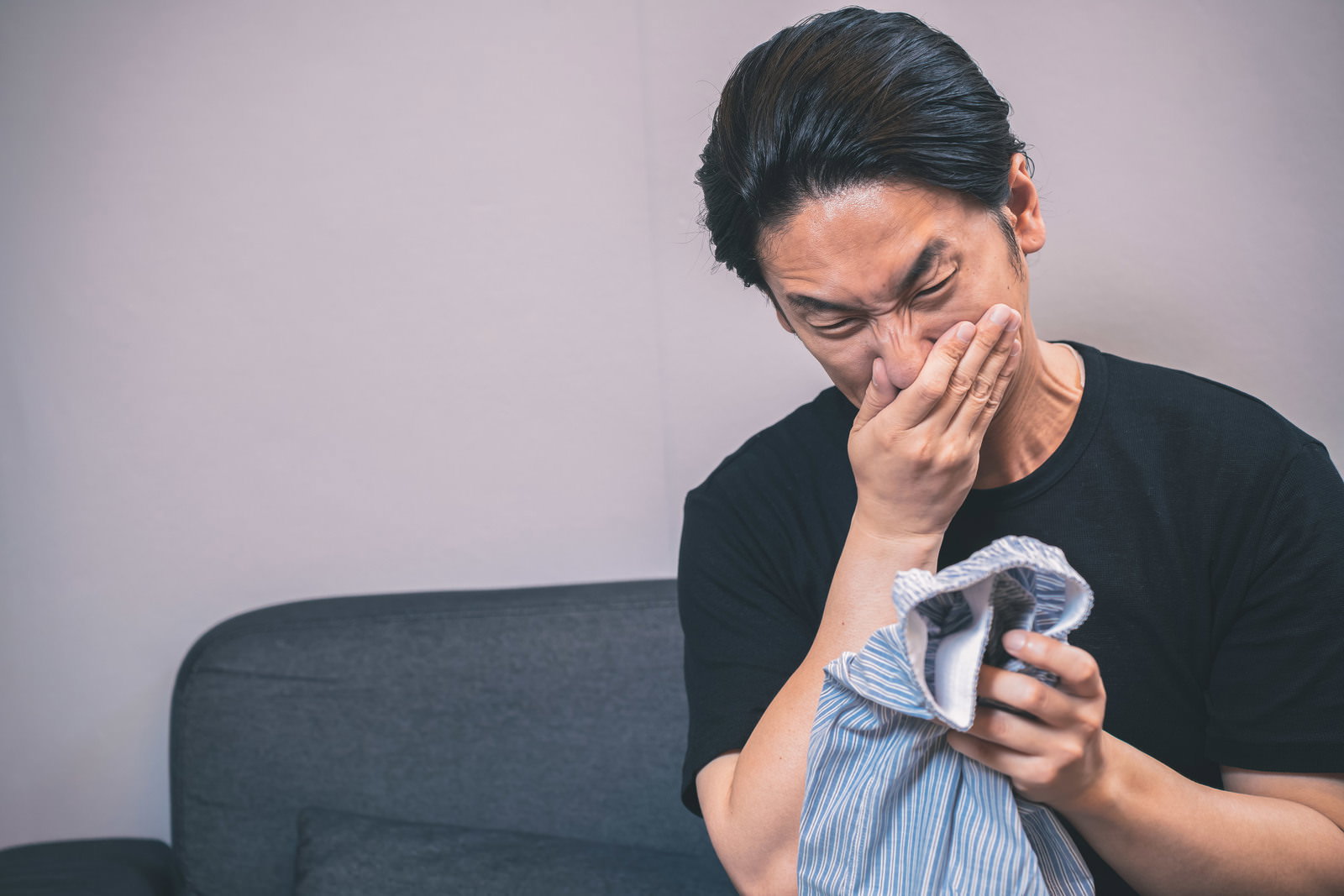 ソファに座り手で顔を覆い頭を抱える緑色の長袖を着た男性［モデル：大川竜弥］