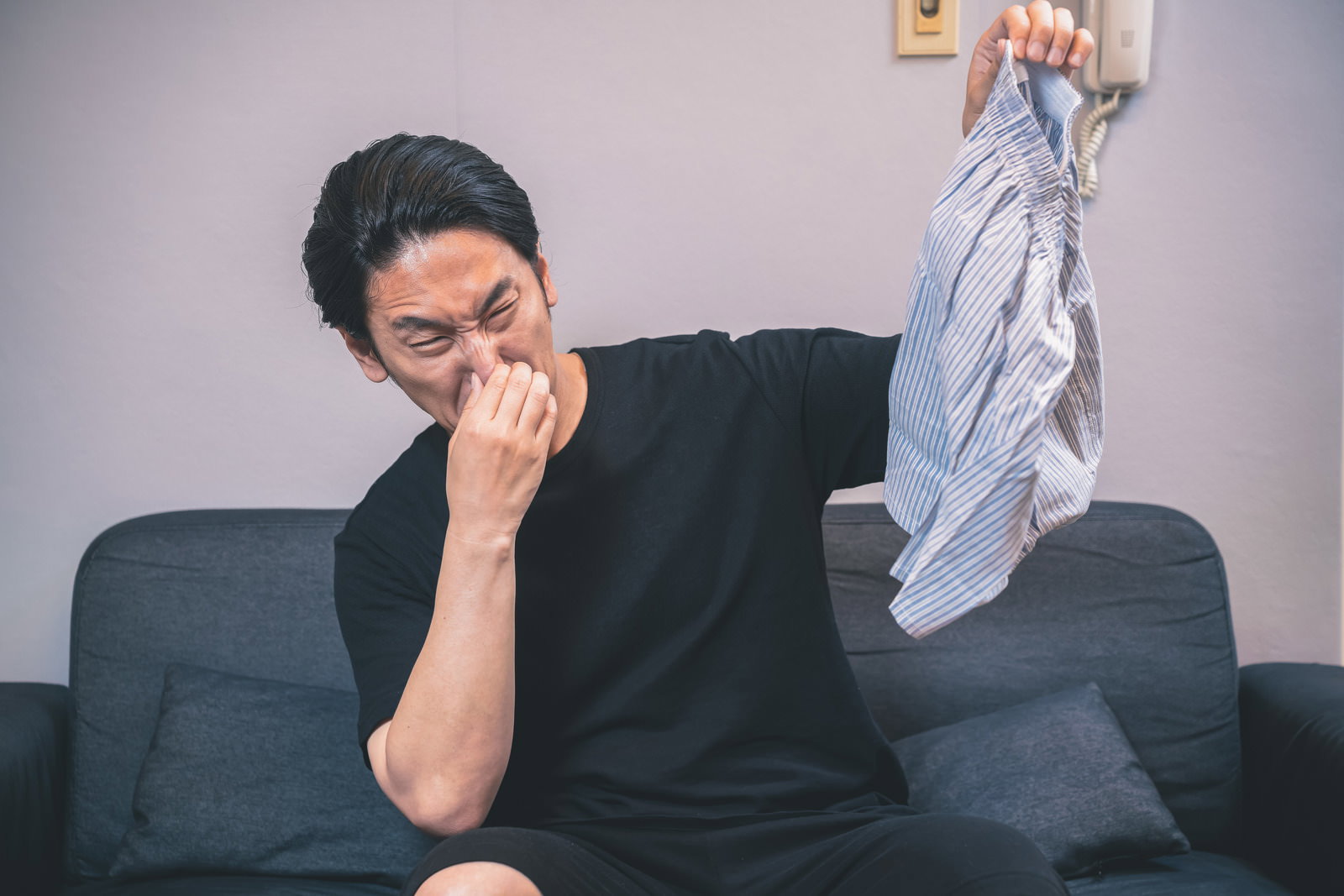 ソファに座り白いパンツのにおいを嗅いで顔を覆う黒髪の男性［モデル：大川竜弥］