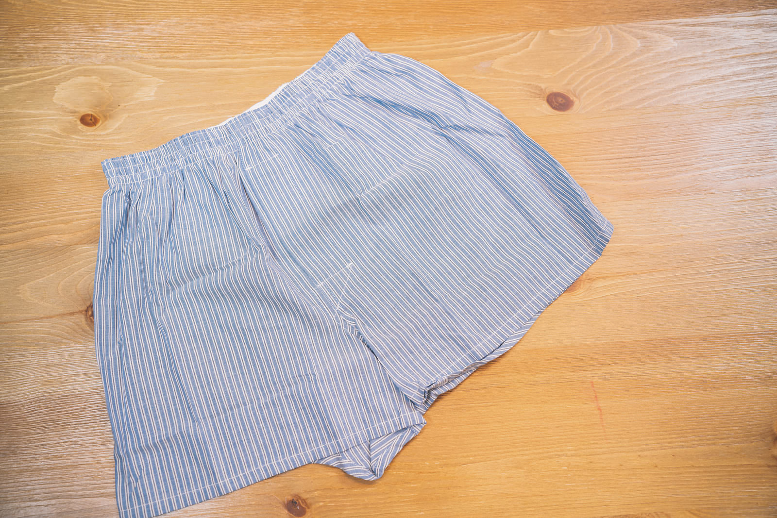 木の机の上に置かれた薄いブルーとホワイトのストライプ柄のトランクス