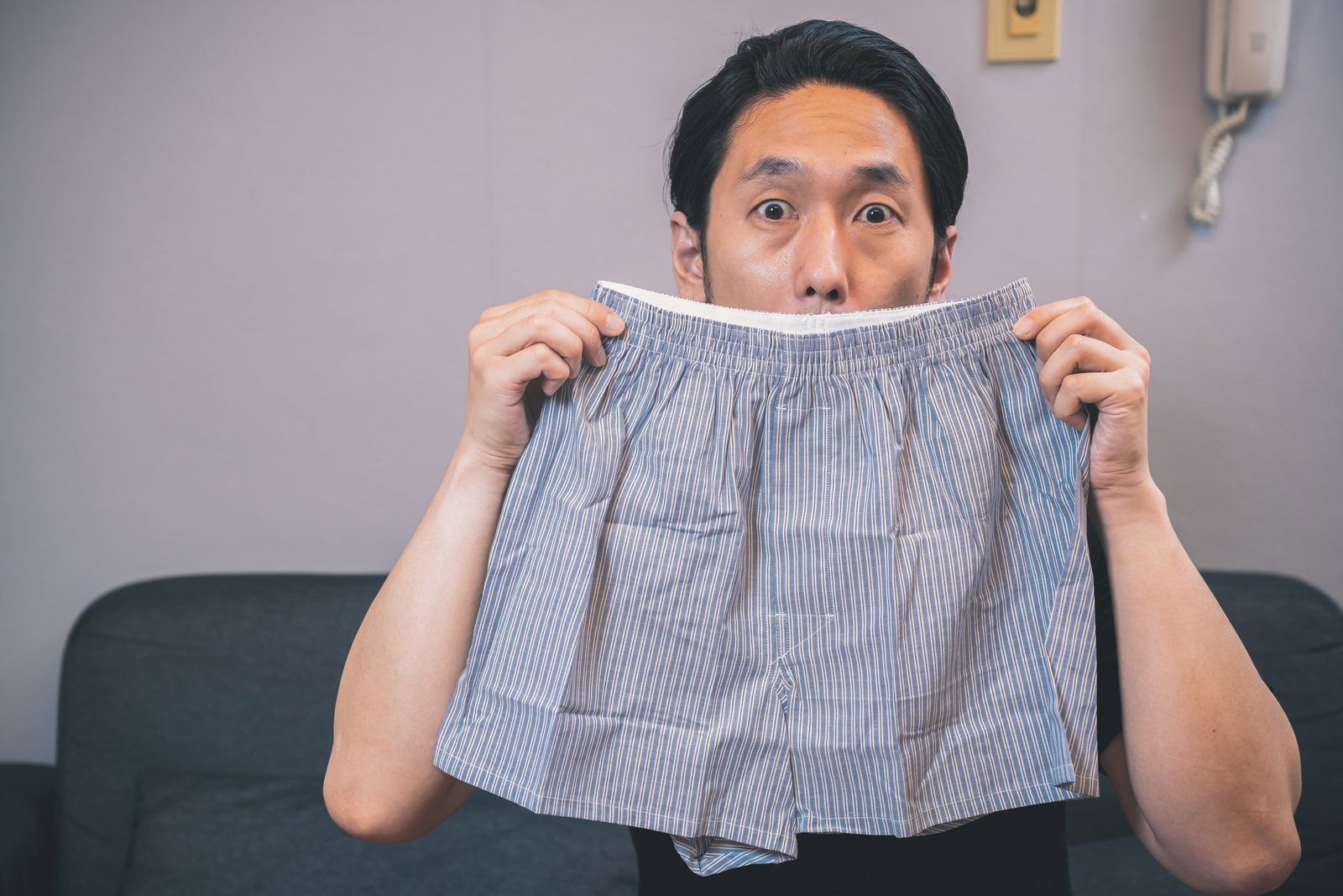 ソファに座ってトランクスのにおいを嗅いでいる男性［モデル：大川竜弥］