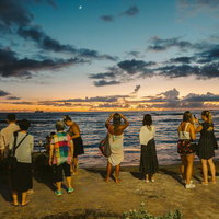 海沿いの海岸で日の出を眺める外国人観光客の写真