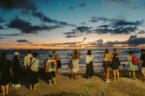 海沿いの海岸で日の出を眺める外国人観光客