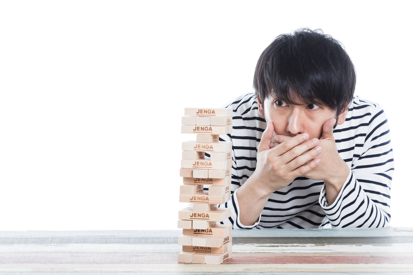 ブロックを抜き取ろうとする男性がジェンガの塔を見つめ、口元に手を当てて緊張した表情［モデル：大川竜弥］