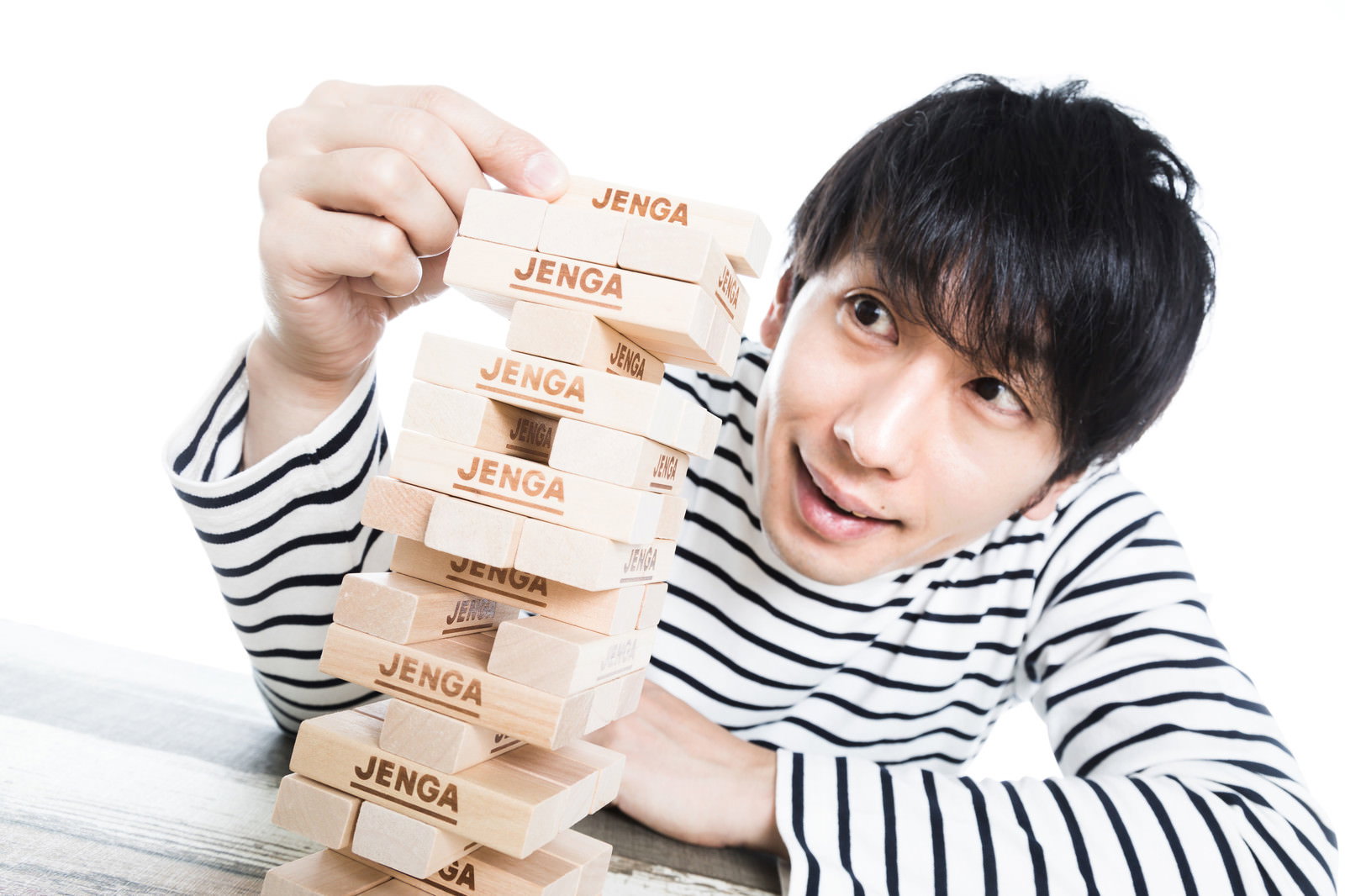 ジェンガのブロックを慎重に抜き取ろうとする男性［モデル：大川竜弥］