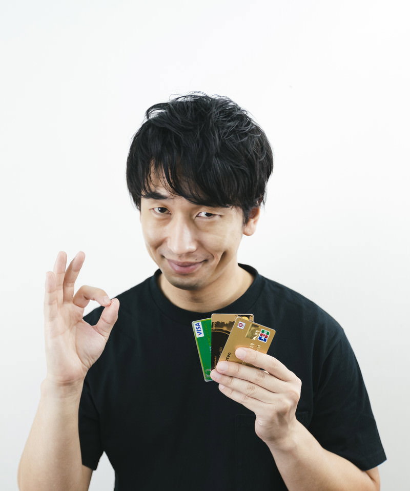 クレジットカードを持ちOKサインを出す黒いTシャツの男性［モデル：大川竜弥］