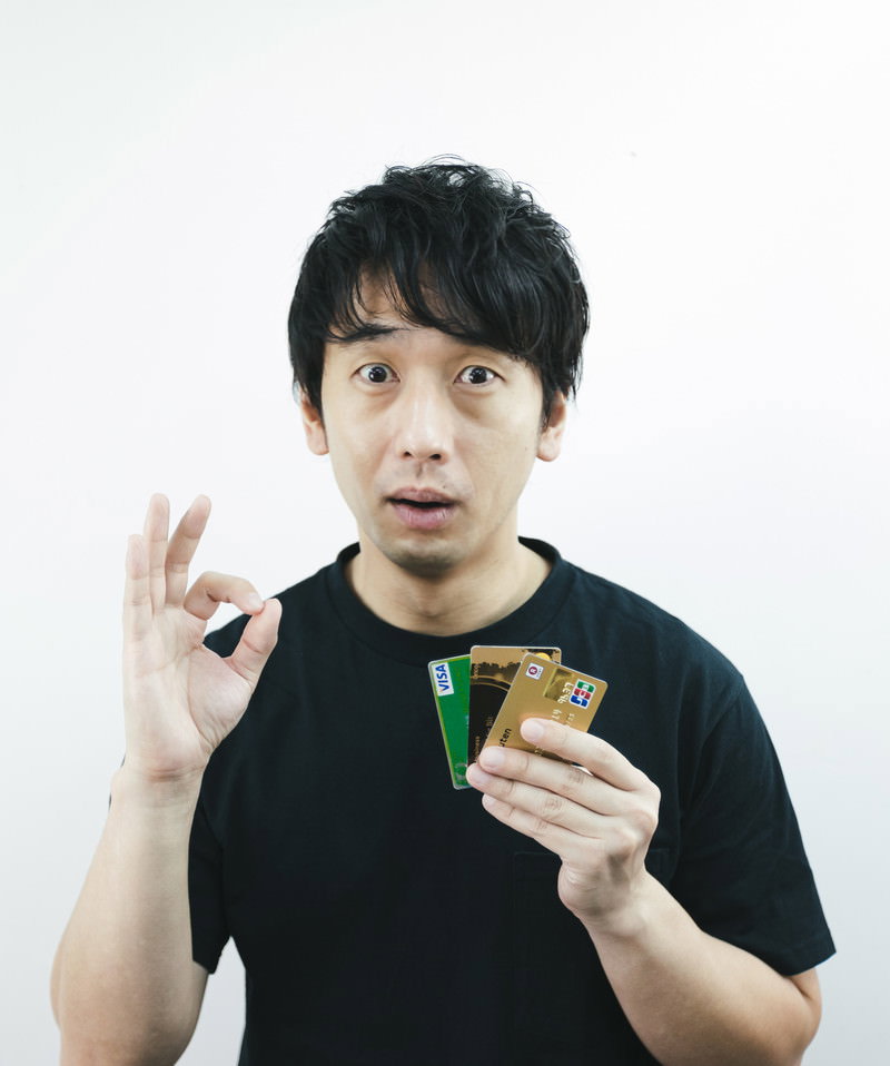 クレジットカードを持ってOKサインをする黒いTシャツの男性［モデル：大川竜弥］