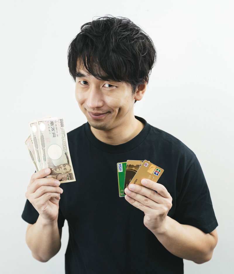 現金とクレジットカードを両手に持つ黒シャツの男性［モデル：大川竜弥］