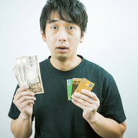 現金とクレジットカードを持つ男性が支払い方法を比較検討の写真