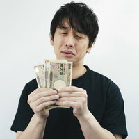 今月も生活がピンチ、一万円札を手に困った表情の男性の写真