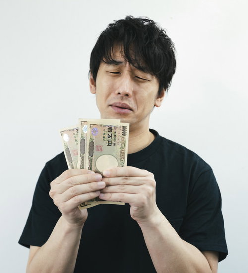 今月も生活がピンチ、一万円札を手に困った表情の男性