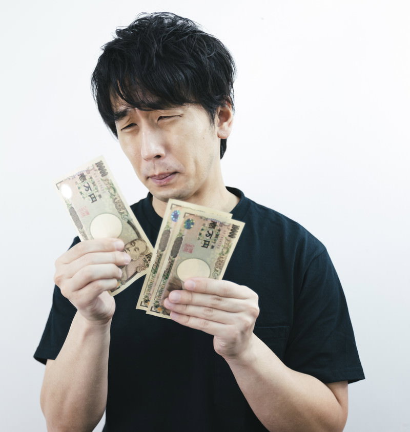千円札を持って困った顔をする男性［モデル：大川竜弥］