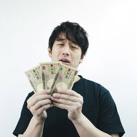月末お金がなくて困った男性が手に持つ現金と困惑した表情の写真