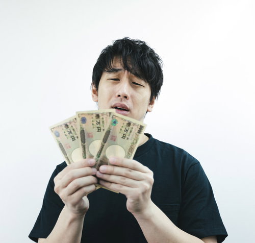 月末お金がなくて困った男性が手に持つ現金と困惑した表情