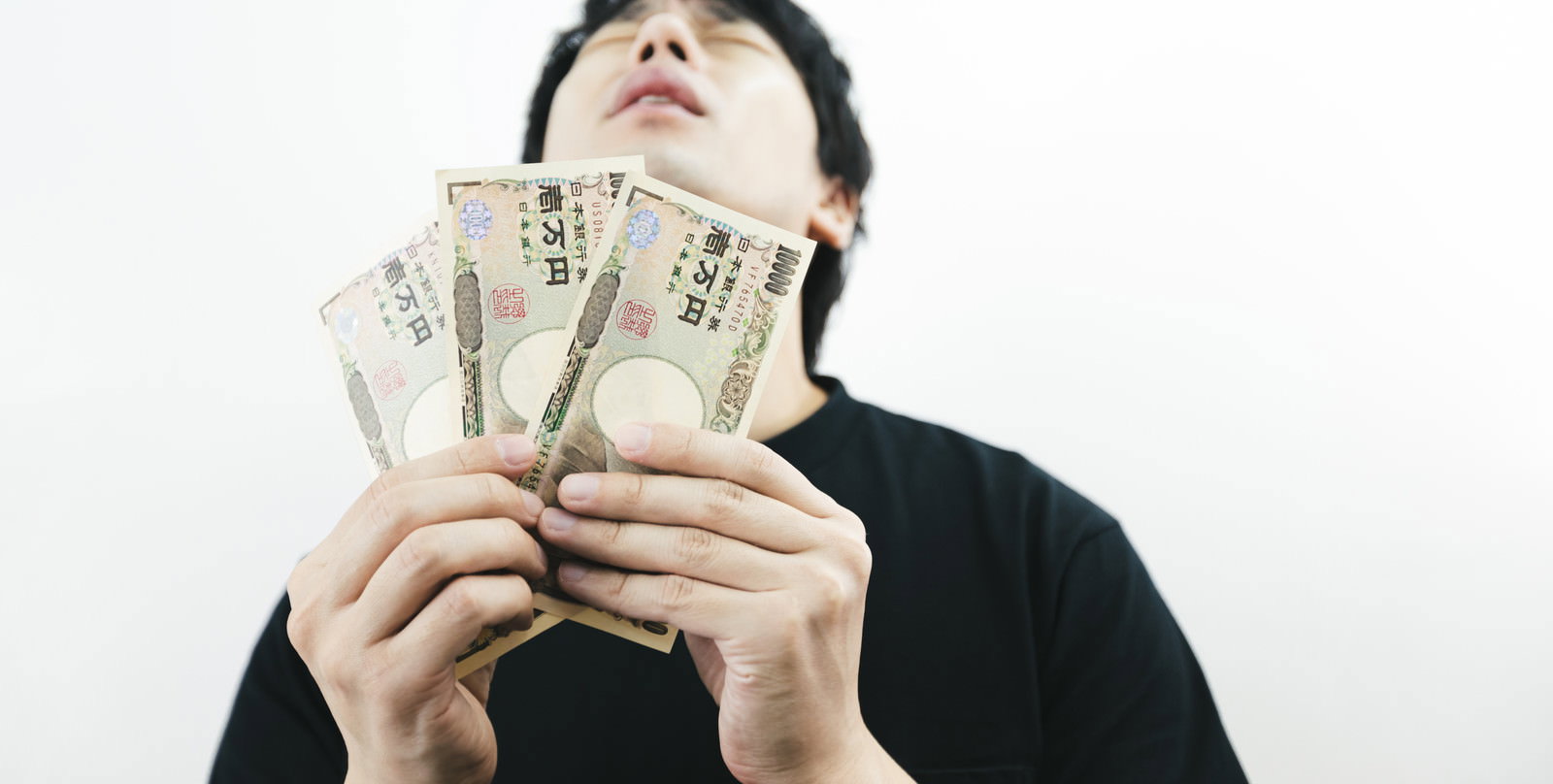 一万円札を両手で持って上を向いて喜ぶ男性［モデル：大川竜弥］