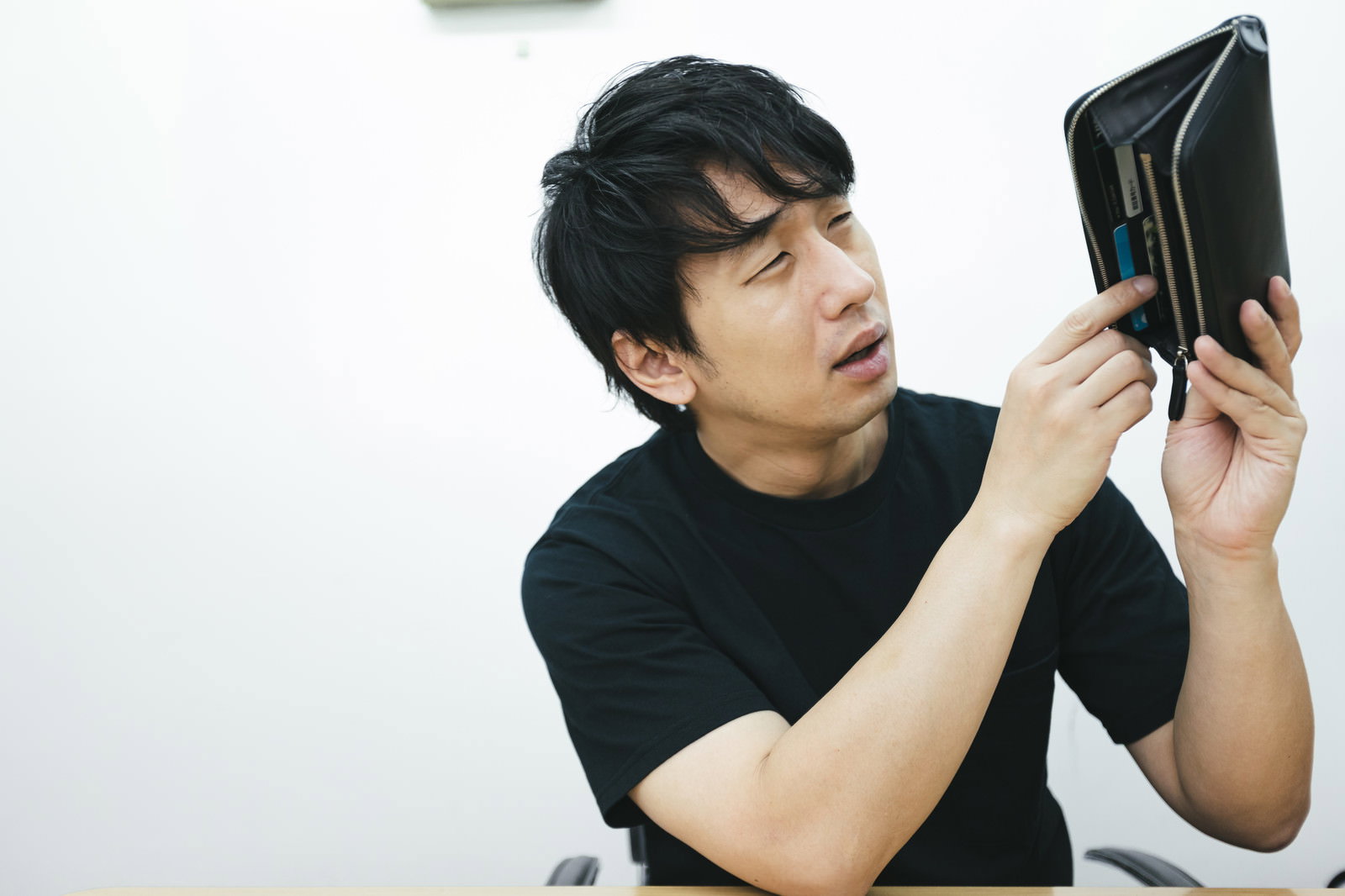 空の財布を開いて中身を確認している黒い服を着た男性［モデル：大川竜弥］