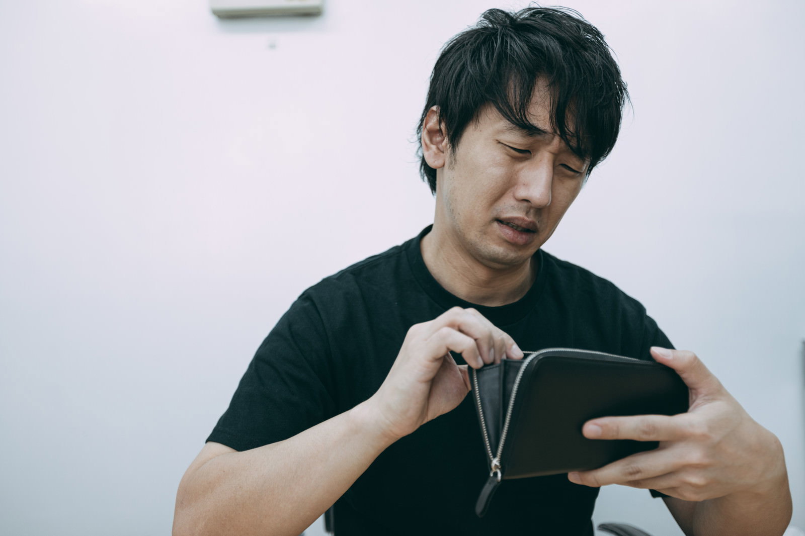 黒いTシャツを着た男性が財布を開いて中身を確認している［モデル：大川竜弥］