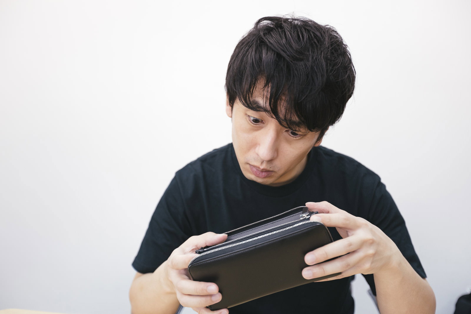 黒い財布を両手で持ち下を向いて中身を見つめる男性［モデル：大川竜弥］