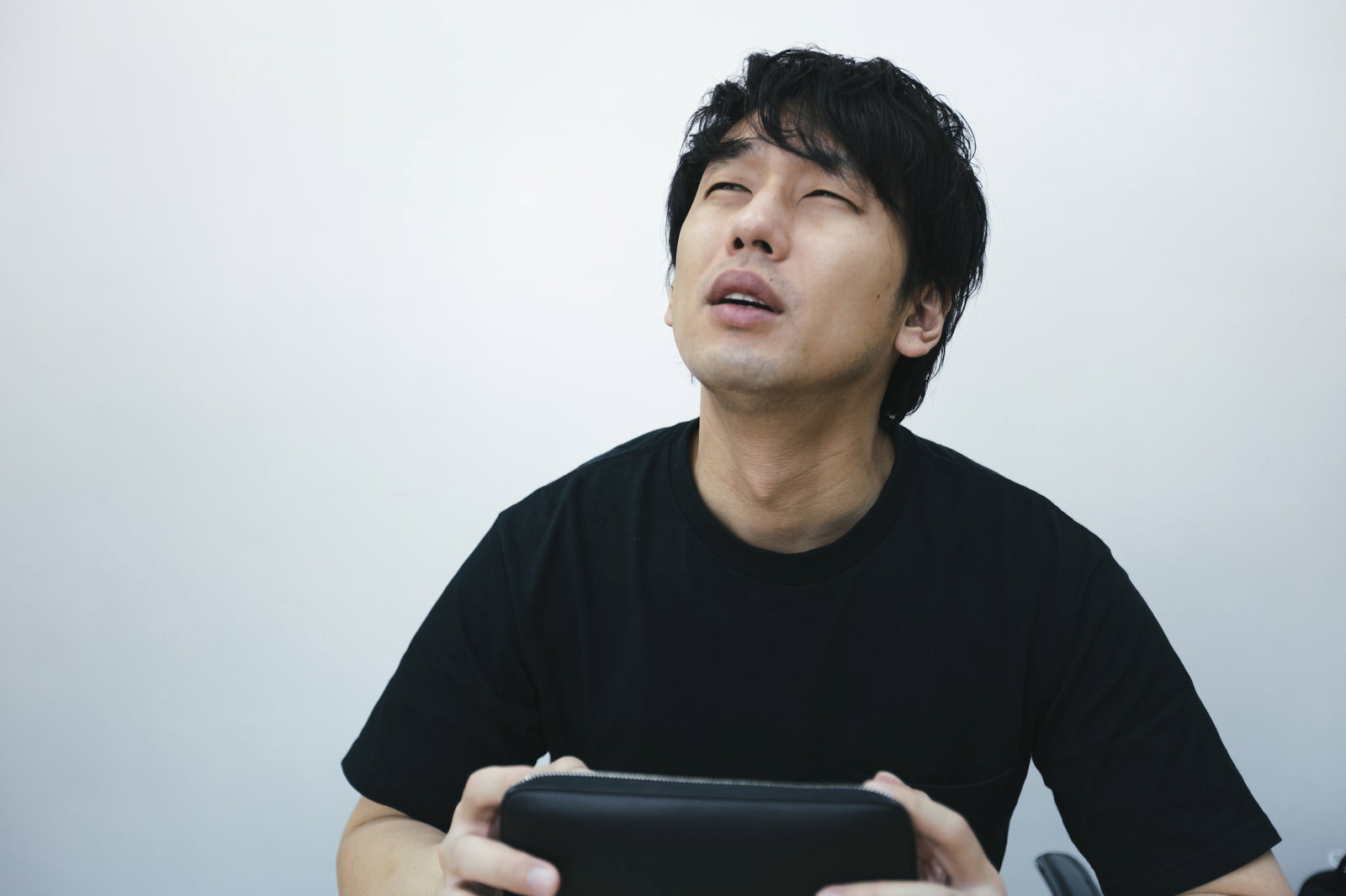 空の財布を持って困った表情で上を見上げる黒いTシャツの男性［モデル：大川竜弥］