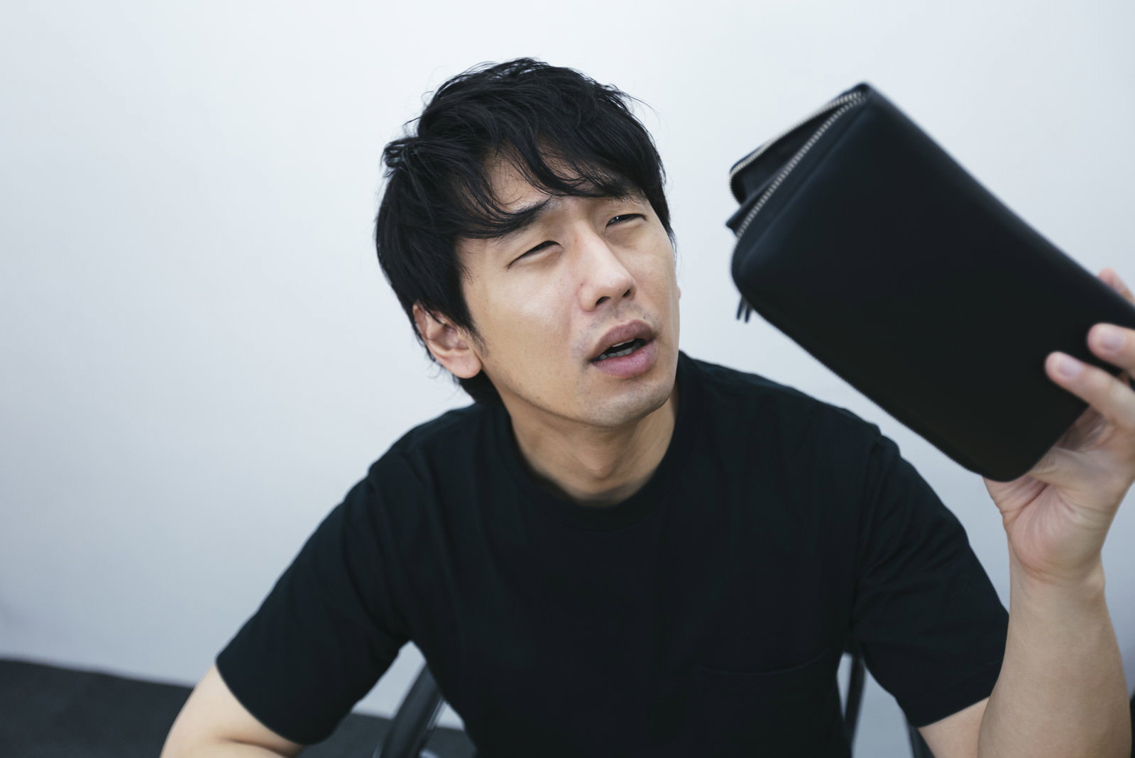空の財布を手に持ち困った表情を浮かべる黒い服の男性［モデル：大川竜弥］