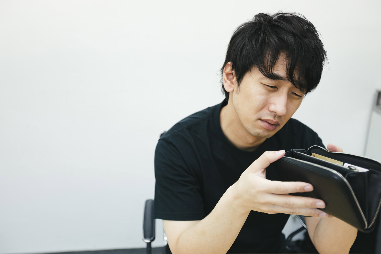 空の財布を手に持ち困った表情を浮かべる男性［モデル：大川竜弥］