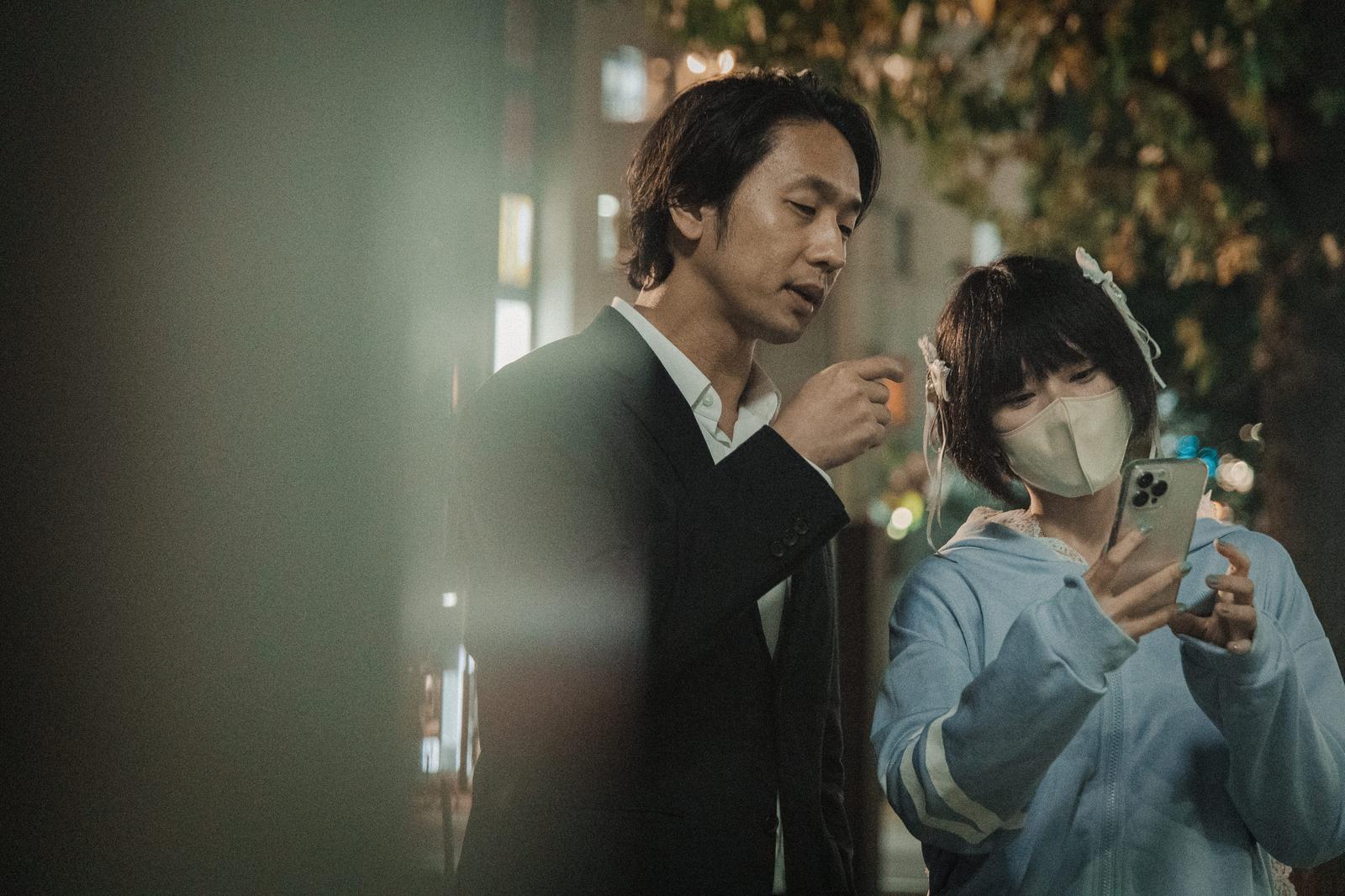 スマートフォンを持ちながら男性と話すマスク女子と中年男性［モデル：大川竜弥 緋真煉］
