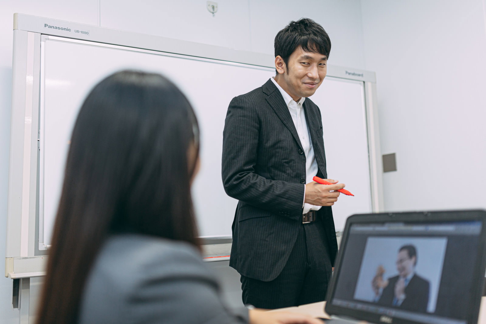 会議室でホワイトボードを使ってプレゼンテーションをするスーツ姿の男性［モデル：大川竜弥］